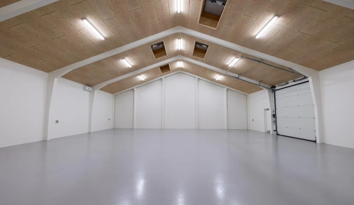 Hallen på Marktoften 7B med hvide vægge, træbetonloft, ovenlys og to porte